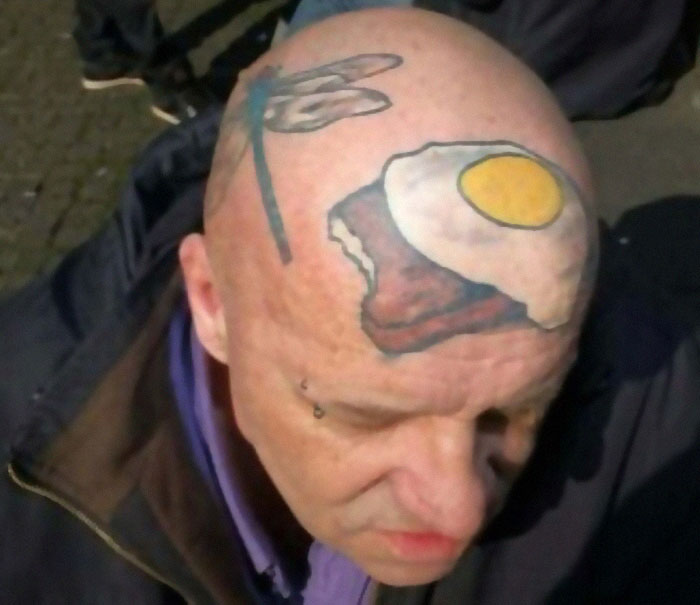 Bald man with ink fail tattoo of a fried egg and toast on his head, showcasing permanent tattoo regrets.