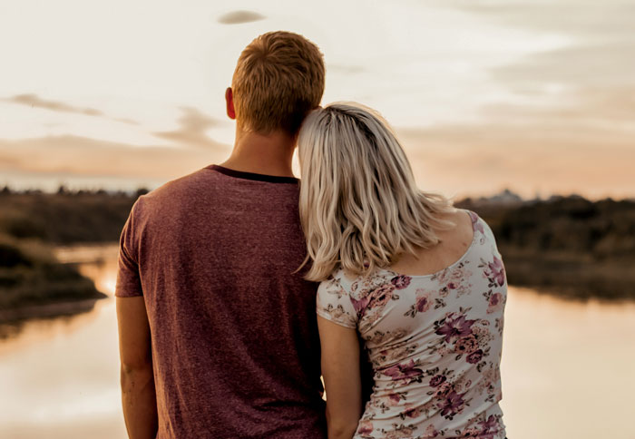 Couple embracing by the river at sunset, reflecting on dumb partner moments in their relationship.
