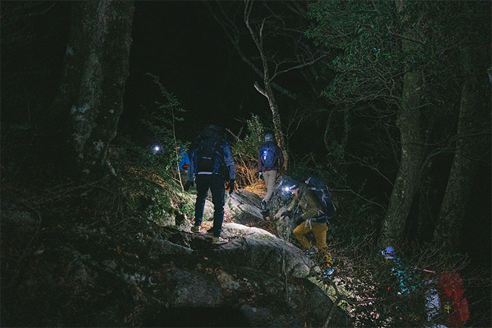 Group of hikers with headlamps navigating a dark forest trail at night during a scary camping and hiking adventure.