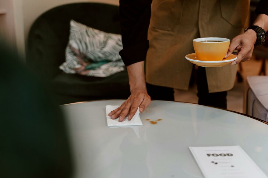 Person cleaning a table with a cloth while holding a cup of coffee, demonstrating practical psychology tricks in action.