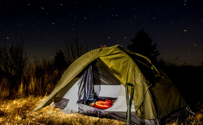 Tent pitched in the woods at night with camping gear, evoking terrifying things people saw or heard in the woods.