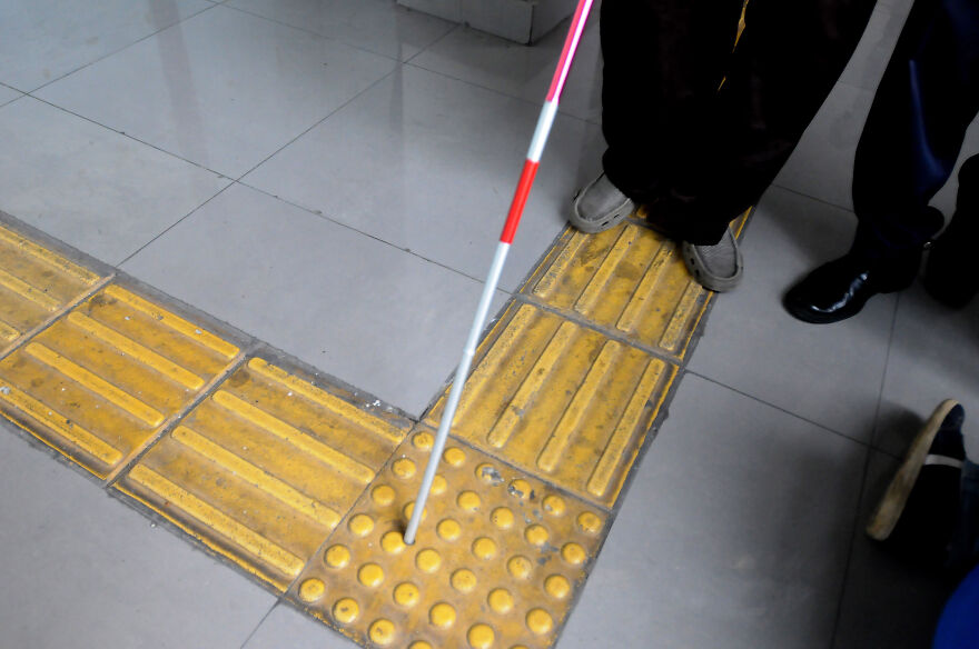 White cane pointing to tactile paving on floor, showing curious objects with origins designed for accessibility navigation.