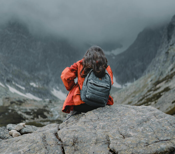 Hiker wearing a red jacket and gray backpack sitting on a rock in a foggy mountainous landscape during a scary camping trip.