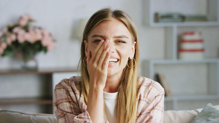 Young woman smiling and covering her face, representing secrets women don't tell men in a casual home setting.