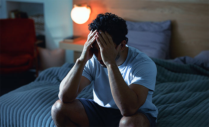 Man sitting on bed with head in hands, looking distressed after wife admits to cheating multiple times for variety.