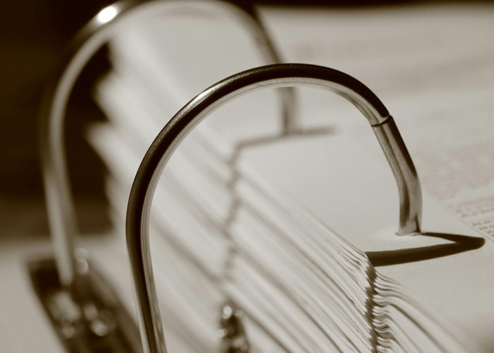 Close-up of a large stack of paper held by metal binder rings, illustrating organized reasons people ended up in ER.