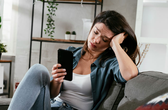 Woman sitting on a couch, looking distressed while holding a phone, representing people who lost a friend and shared stories.