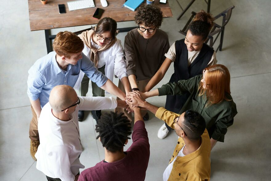 Diverse group of young professionals joining hands in office, symbolizing teamwork and psychology tricks for real-world situations.
