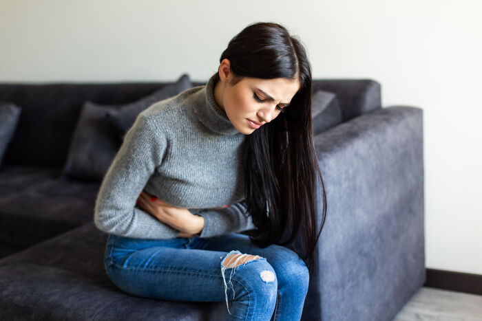 Woman holding abdomen in discomfort sitting on couch, highlighting misconceptions about common women's health issues.