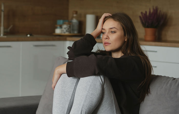 Mulher sentada no sofá parecendo pensativa e preocupada, refletindo sobre testes secretos de paternidade e questões de confiança em casa Mulher sentada no sofá parecendo pensativa e preocupada, refletindo sobre testes secretos de paternidade e questões de confiança em casa