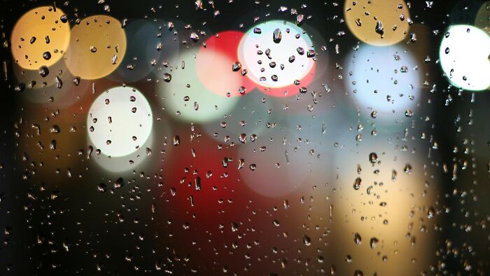 Raindrops on a window with blurred colorful lights in the background, evoking childhood memories and common experiences.