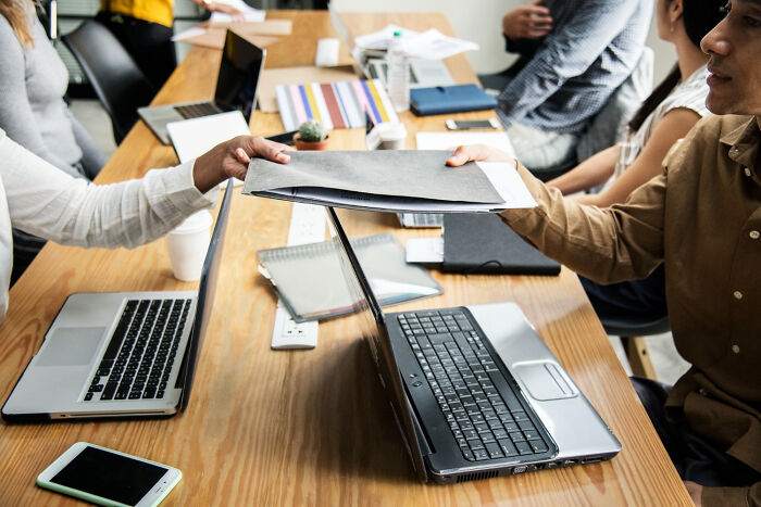 Person handing documents over a laptop in a meeting, illustrating karma hitting those who try to sabotage others.