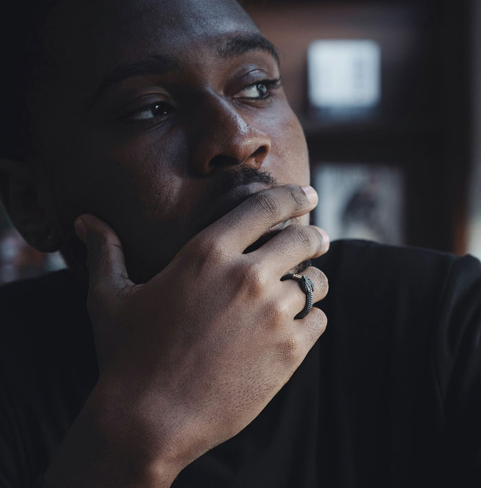 Homem com expressão pensativa vestindo camisa preta e anel, contemplando teste de paternidade secreto para preocupações com bebês recém-nascidos. Homem com expressão pensativa vestindo camisa preta e anel, contemplando teste de paternidade secreto para preocupações com bebês recém-nascidos.