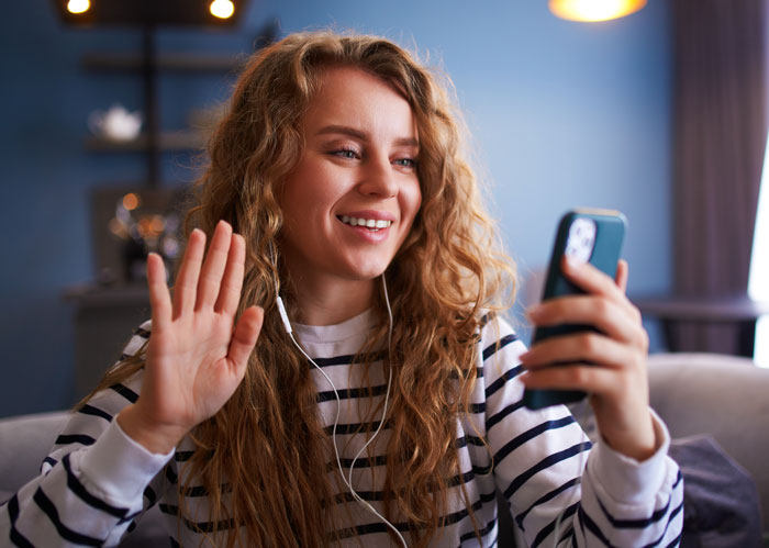 Young woman smiling and waving during a video call, parents are mad daughter didn&rsquo;t tell them about house purchase.