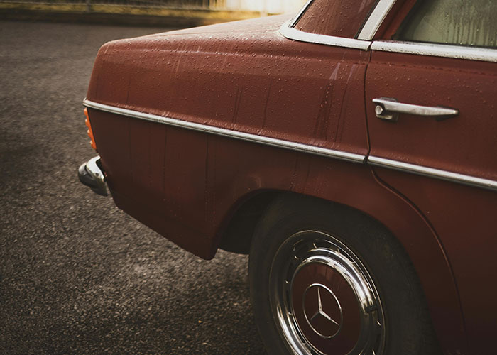 Vintage red car parked on wet asphalt, illustrating unserious reasons why people ended up in the ER after tripping.