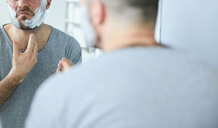 Man shaving and looking in bathroom mirror, illustrating weird and adorable relationship lessons about men.