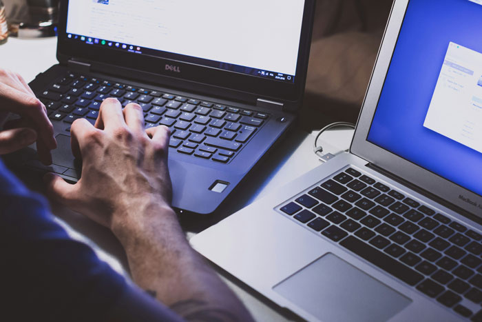 Person typing on laptop keyboard beside another open laptop, illustrating corporate secrets and customer insight research.