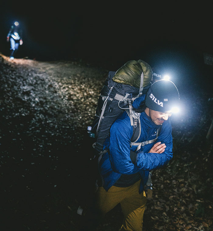 Two hikers wearing headlamps walking through dark woods at night, capturing a feeling of terrifying experiences in nature.