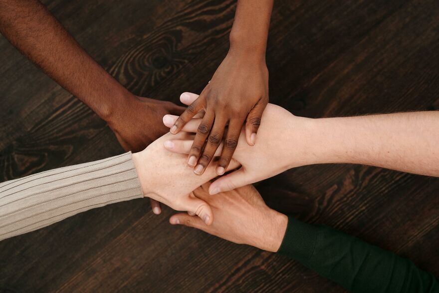 Diverse group showing small behaviors that make people like you more by joining hands in unity over a wooden table.