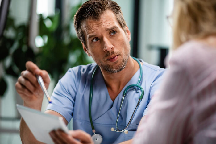 Male doctor in blue scrubs talking to a woman, addressing common health concerns women thought were normal.