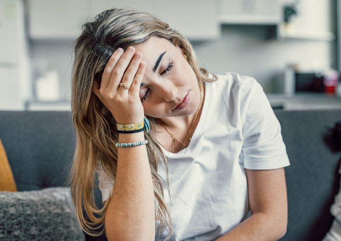 Young woman looking stressed on couch, symbolizing parents mad daughter didn&rsquo;t tell them about buying a house secretly.
