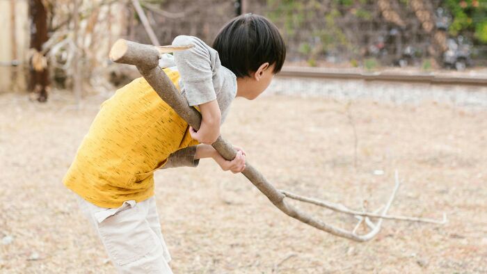 Child playing outdoors holding a large stick, illustrating common activities everyone thought were unique as a kid.