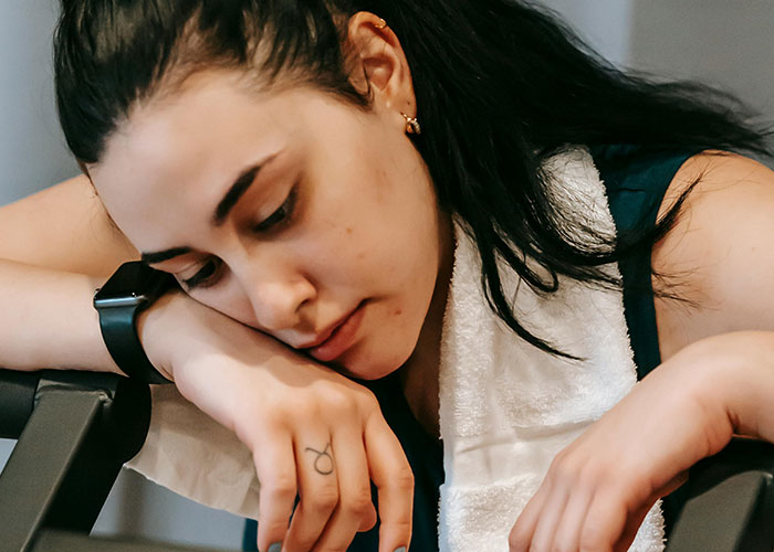 Young woman resting with towel after workout, looking tired and recovering from an unexpected injury at the gym.