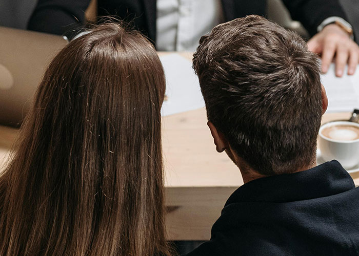 Couple sitting closely at a table with a third person across, illustrating a messy love triangle dynamic.