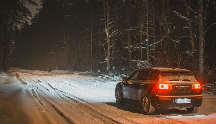 Car with red tail lights on snowy road in dark woods, evoking eerie and terrifying forest instincts.