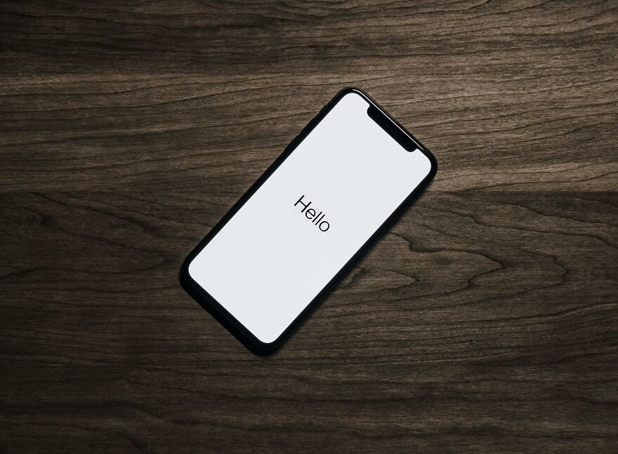 Smartphone on a dark wooden surface displaying the word Hello, symbolizing small behaviors that make people like you more.