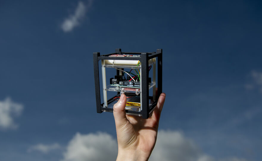 A hand holding a curious object with electronic components against a blue sky, highlighting its dazzling origins.