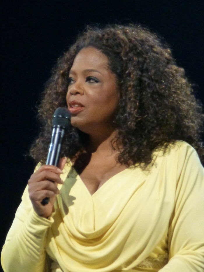 Woman with curly hair in a yellow dress speaking into a microphone, illustrating celebrities people used to like but now hate.