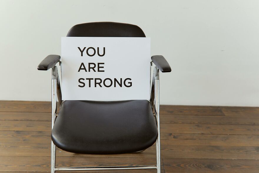 Black chair with a sign reading you are strong placed on wooden floor showing small behaviors that make people like you more.