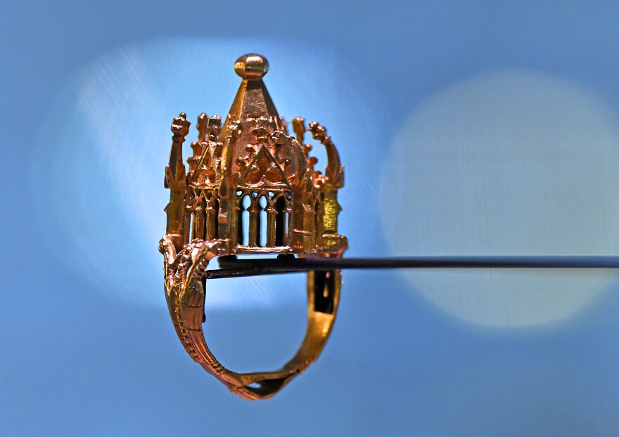 Intricately designed golden ring resembling a miniature cathedral, showcasing curious objects with dazzling origins.