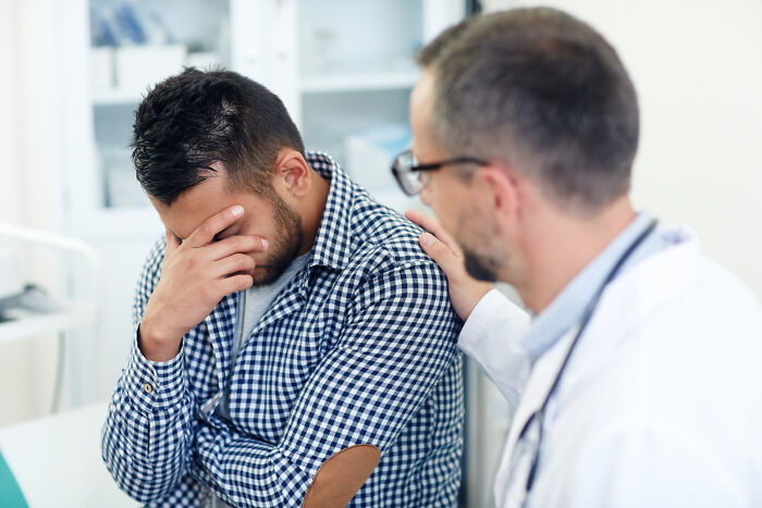 Doctor comforting stressed male patient in clinic, illustrating things doctors prefer to hide from patients.