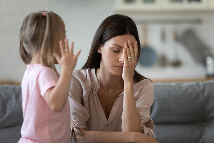 Stressed woman covering face while child raises hand, illustrating tough reasons people stay in a relationship despite hating partner.