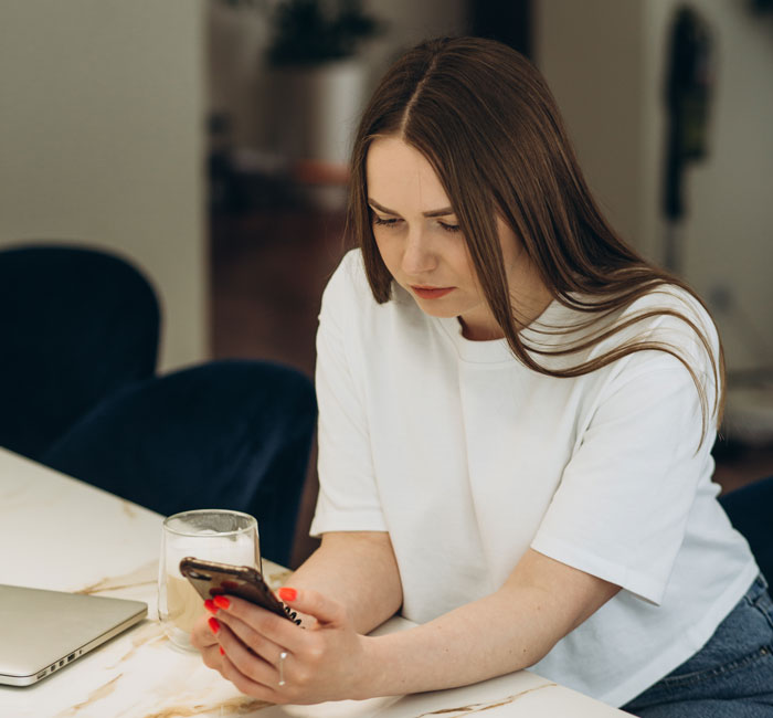 Young woman looking at her phone with concern, reflecting parents mad daughter didn&rsquo;t tell them she bought a house.
