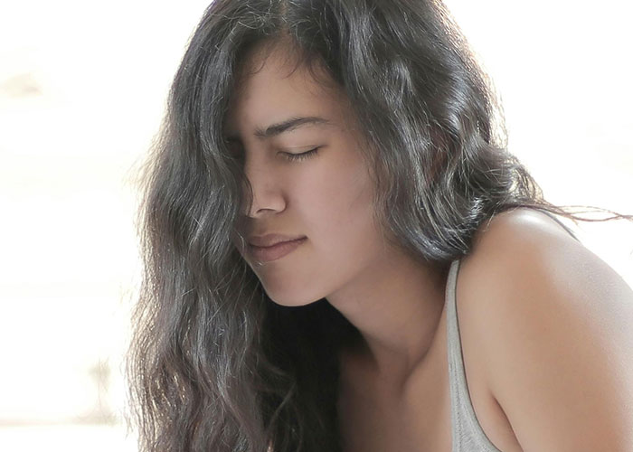 Young woman with long hair wincing in pain, illustrating common reasons people ended up in ER due to tripping over tree roots.