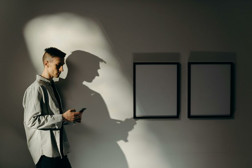 Young man looking at smartphone casting a large shadow on the wall, illustrating practical psychology tricks concept.