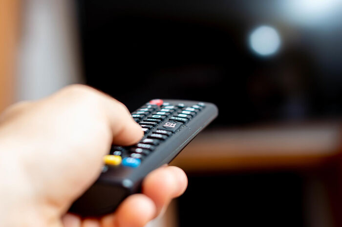 Hand holding a TV remote control pointing at a dark screen, evoking haunted places and spine-chilling experiences.