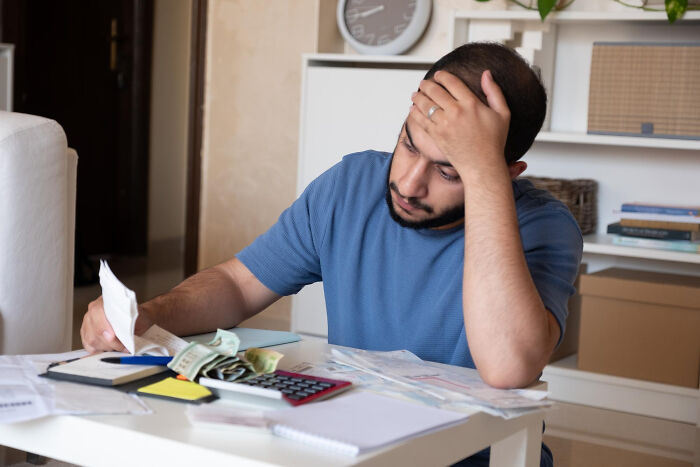 A stressed man sitting at a table with bills and money, illustrating tough reasons for staying in a relationship.