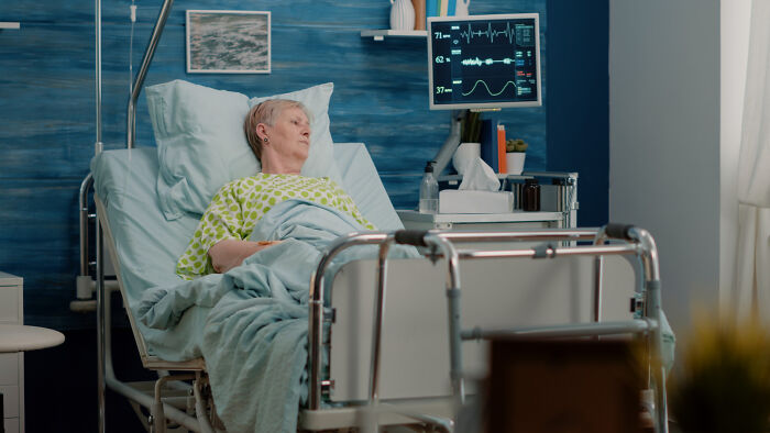 Elderly patient lying in hospital bed with ECG monitor, illustrating doctors hiding medical information from patients.