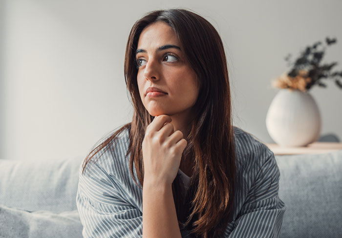 Young woman looking thoughtful on a couch, reflecting on being sneaky while parents are upset she bought a house secretly.