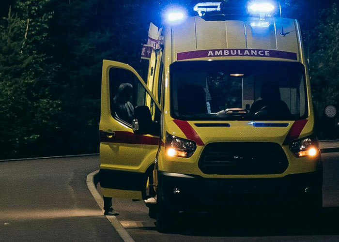 Yellow ambulance with flashing lights parked on a dark road at night, highlighting emergency room and accident response.