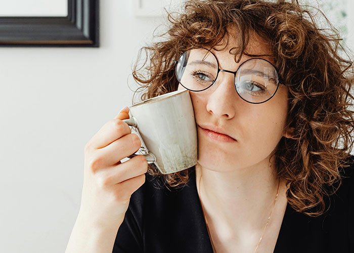 Mulher de cabelos cacheados e óculos segurando uma caneca, refletindo sobre o momento em que seu ex revelou seu verdadeiro eu.