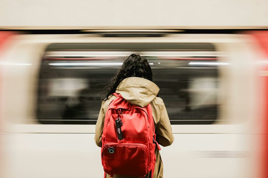 Person with red backpack standing at subway platform with a train passing by, illustrating practical psychology tricks concept.