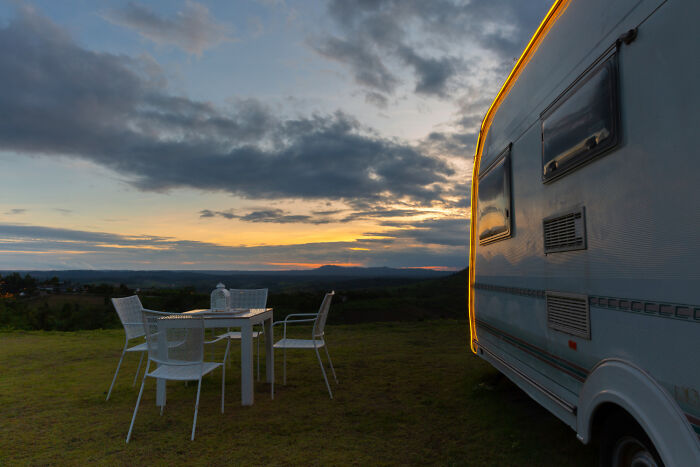 Campervan parked near a table set outdoors at sunset, evoking a sense of bizarre encounters in remote nature settings.