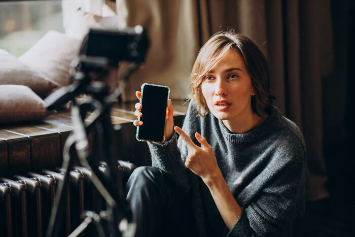 Woman recording a video at home, pointing at her phone, illustrating moments people tried to sabotage others and karma effects.