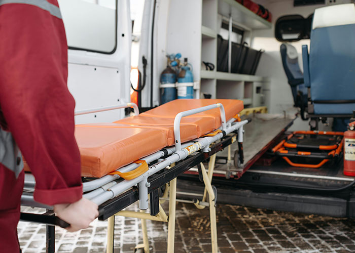Paramedic carrying an empty stretcher into an ambulance after people tripped over a tree root and ended up in ER.