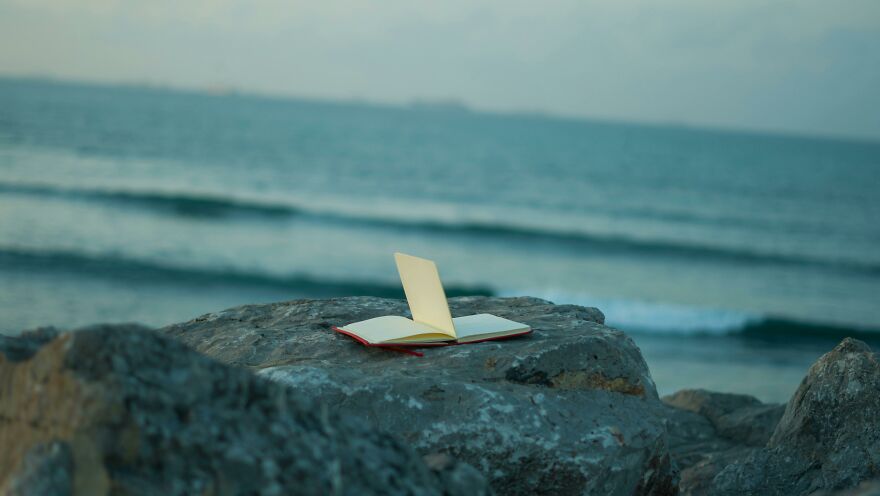 Open notebook on a rocky shore with ocean waves in the background, representing practical psychology tricks.